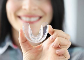 Nightguards / Mouthguards 6 Smiling woman holds transparent plastic mouth guard in her hand. Correction of malocclusion and bruxism concept