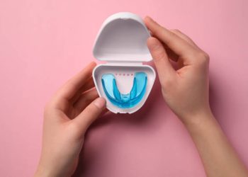 Nightguards / Mouthguards 4 Woman holding container with mouth guard on light pink background, top view. Bite correction